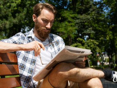 Un jeune homme lit le journal sur un banc.