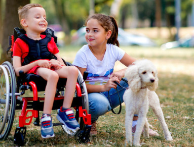 Une fillette joue avec un petit garçon en fauteuil roulant et son chien.