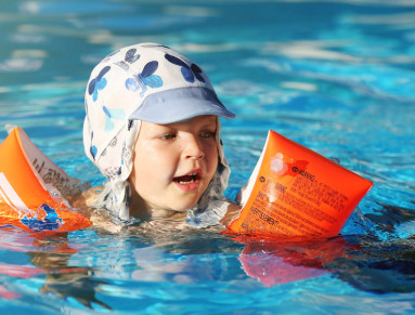 Un enfant portant des brassards se baigne dans une piscine avec ses parents.
