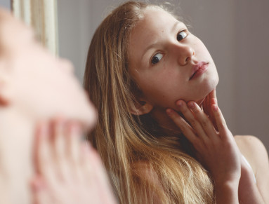 Une adolescente blonde se regarde dans un miroir en penchant la tête