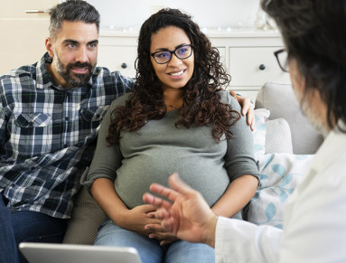 Un couple avec femme enceinte discuter avec un médecin.