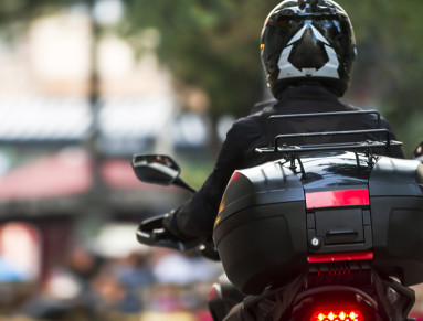 Un motard vêtu de noir et de dos circule en ville