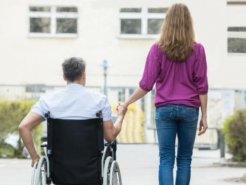 Une femme accompagne son marie en fauteuil roulant lors d'une sortie