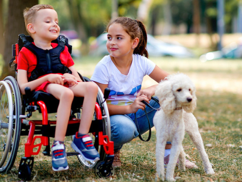 Une fillette joue avec un petit garçon en fauteuil roulant et son chien.