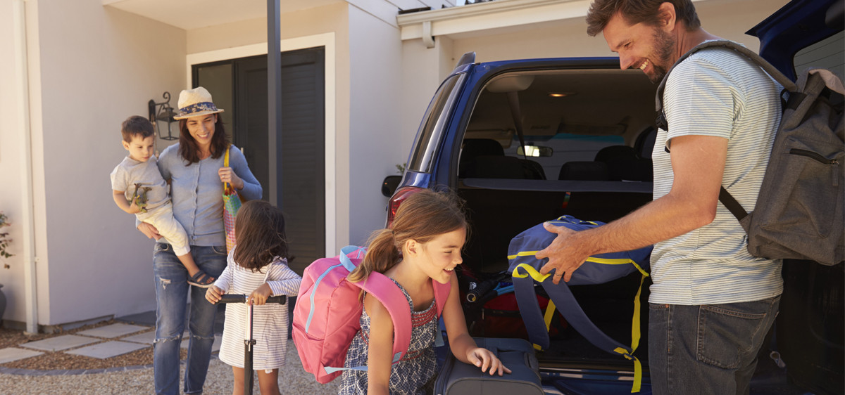 Une famille avec enfants range les valises dans le coffre de leur voiture