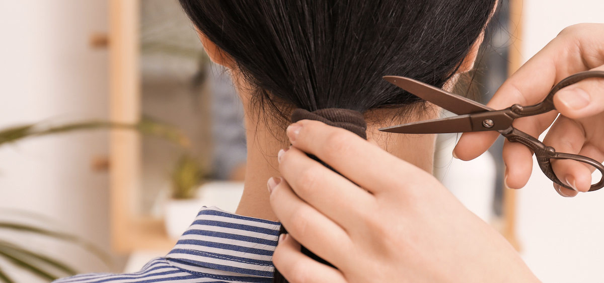 Un coiffeur coupe les longs cheveux bruns d’une jeune femme