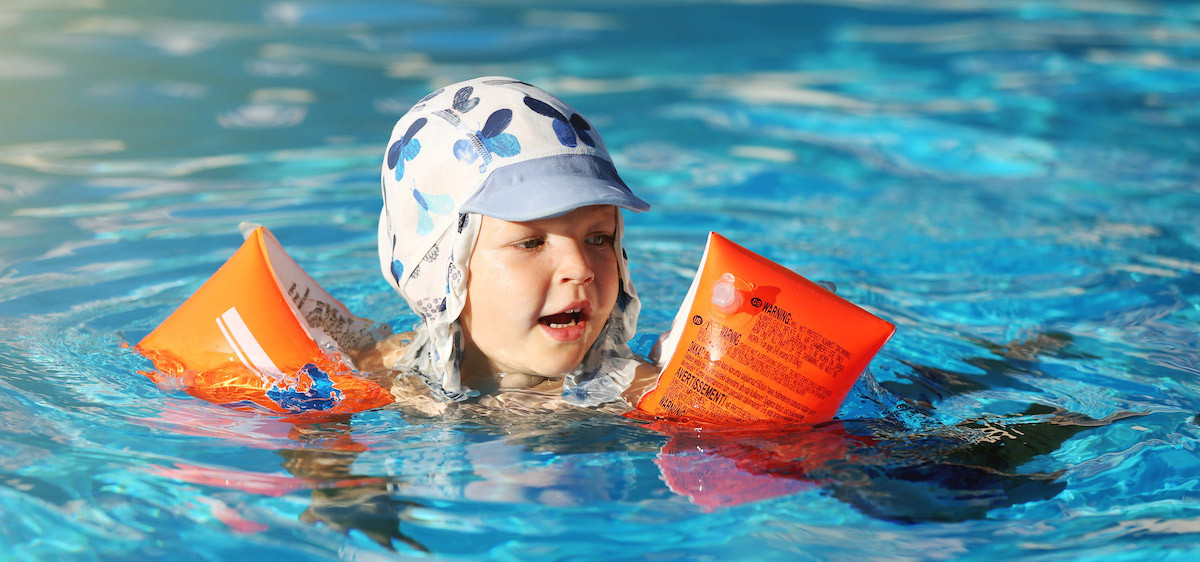 Un enfant portant des brassards se baigne dans une piscine avec ses parents.