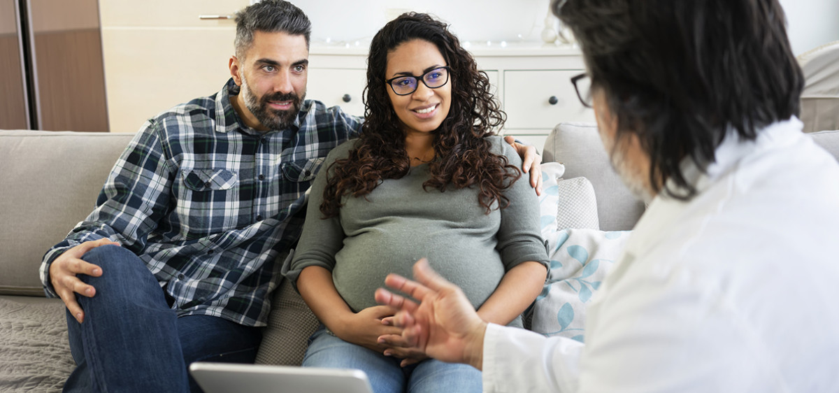 Un couple avec femme enceinte discuter avec un médecin.
